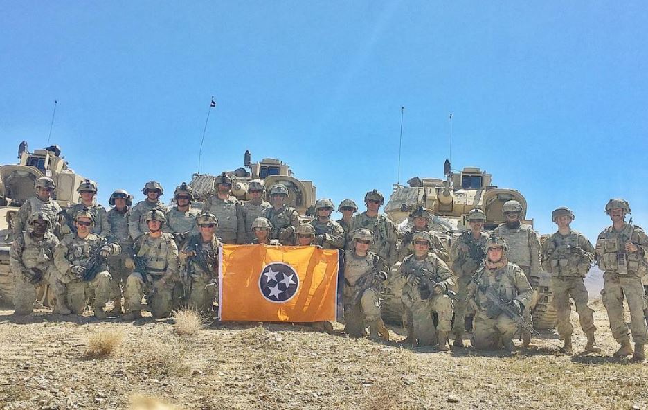 United States of American Soliders in a group holding a Volunteer Traditions Orange Tennessee State Flag. 