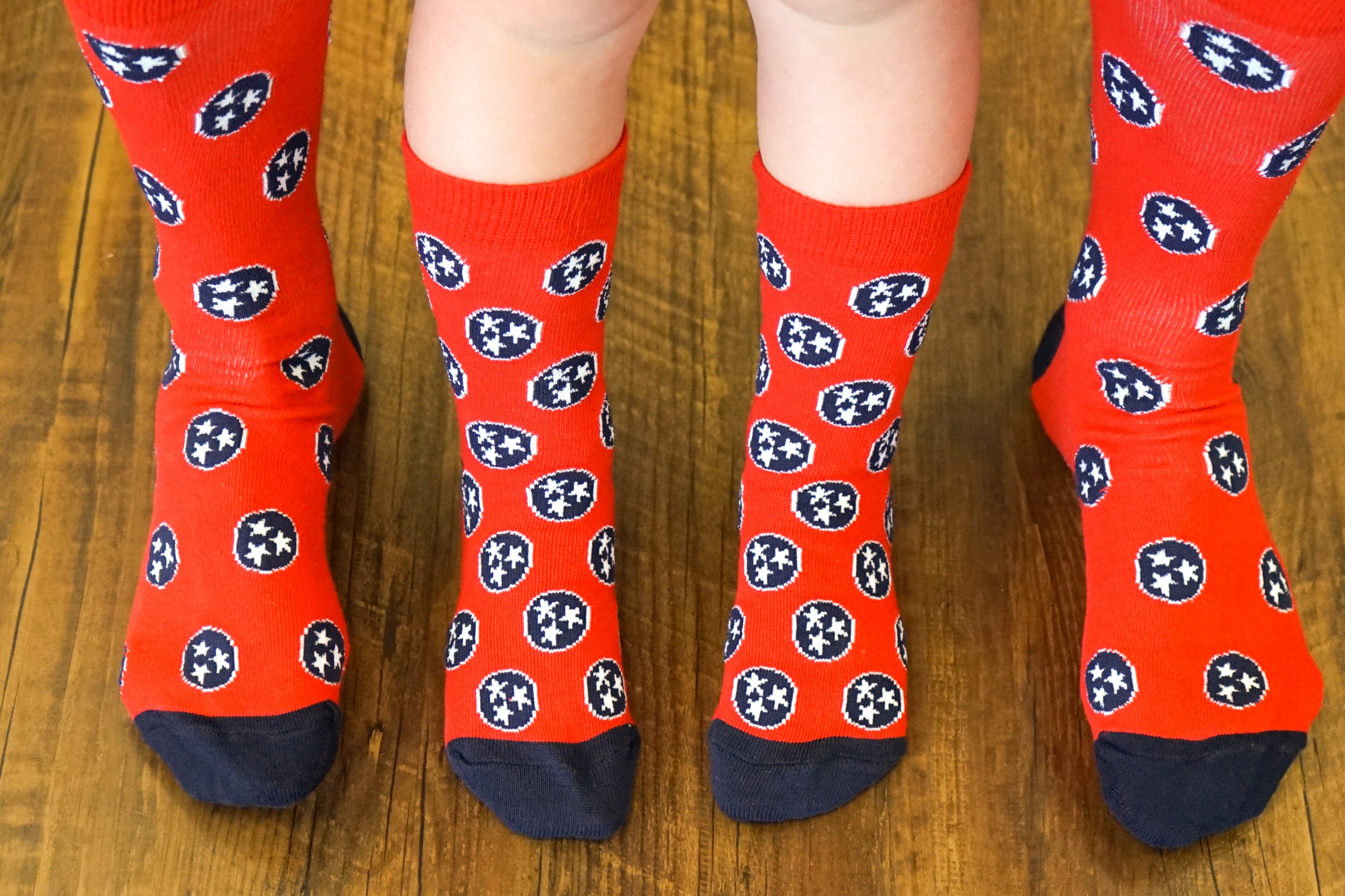 Volunteer Traditions Red and Navy Kid's Tristar Socks on Kids Feet next to Adult Feet for comparison.